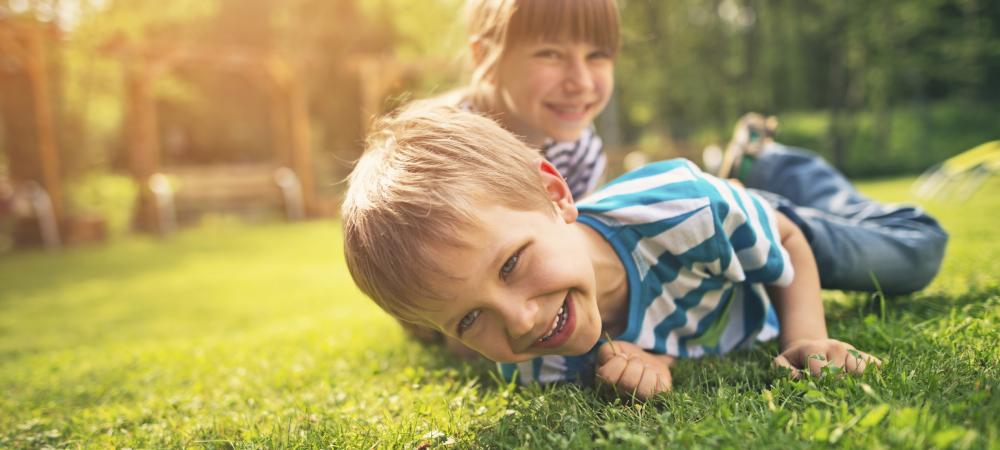 a young boy and a young girl siblings playing in the grass and smiling